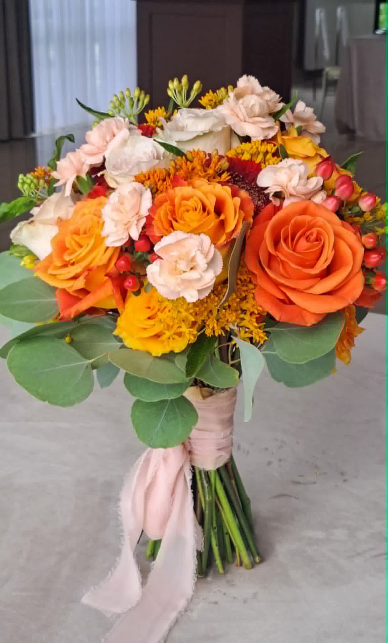 Colorful bridal bouquet with orange and peach roses, yellow dahlia, cream carnations, and greenery