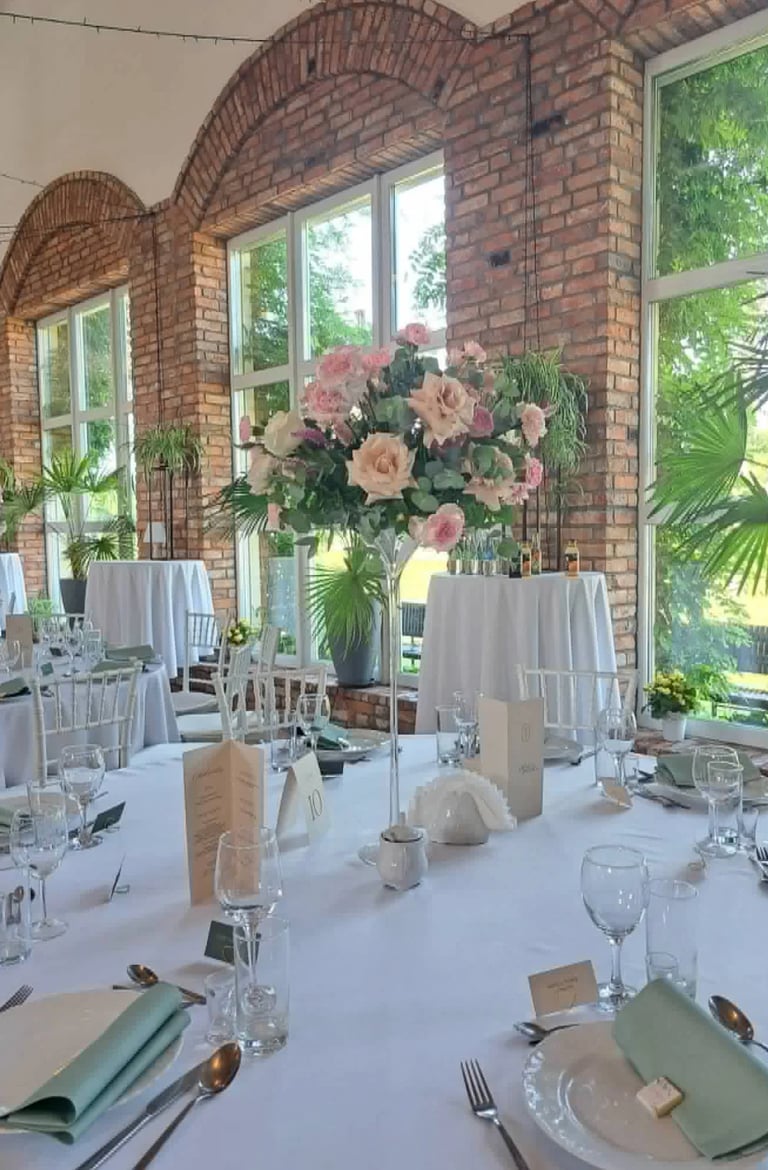 Elegant wedding reception table with white linens, place settings, and pink floral centerpiece in a brick venue with arched windows