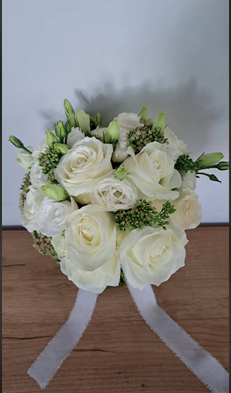 Bridal bouquet of white roses and green hypericum berries tied with lavender ribbons on wooden surface