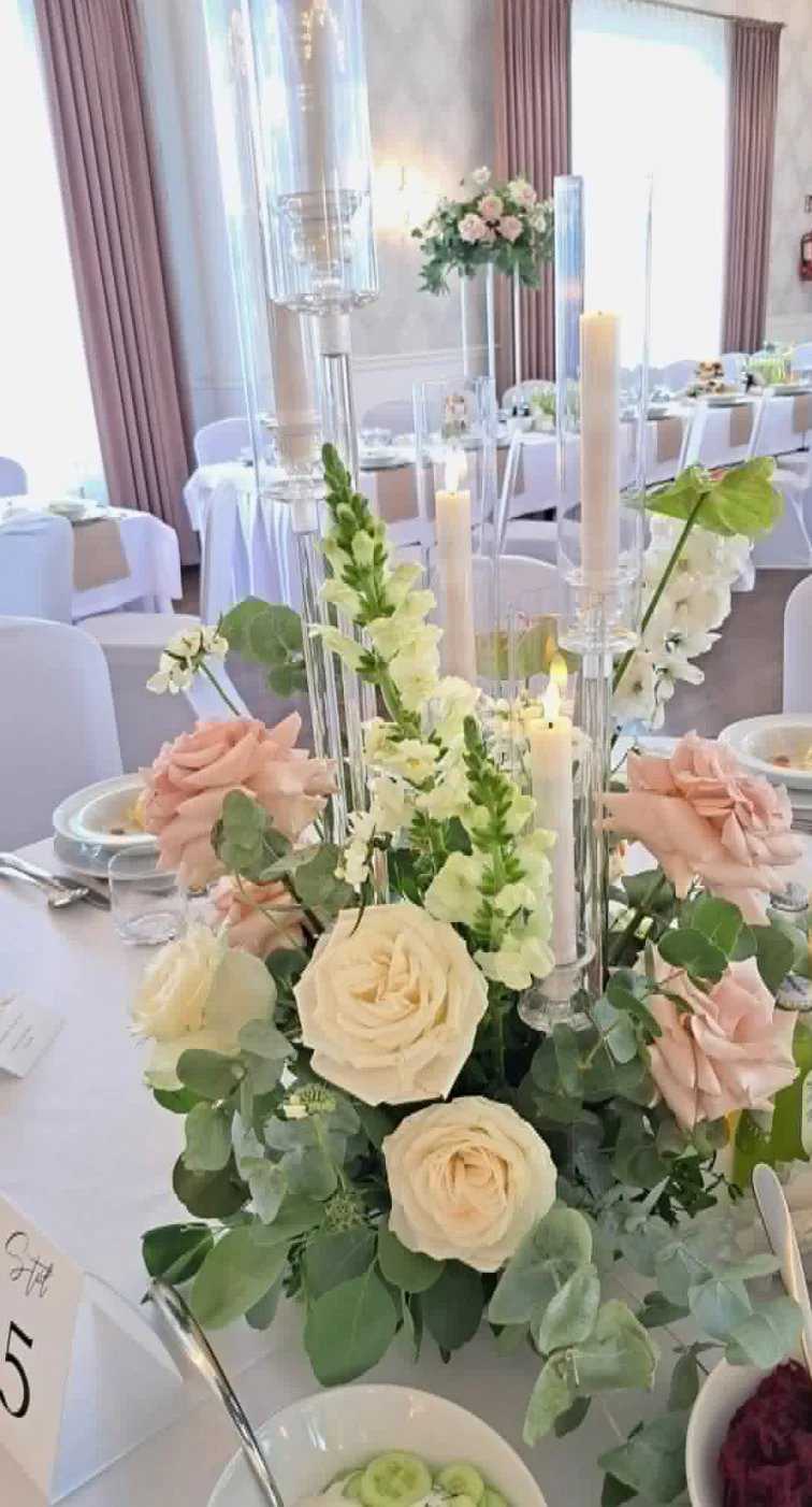 Elegant wedding reception centerpiece with cream roses, peach carnations, and white flowers in clear glass vases with tall candles on white linens
