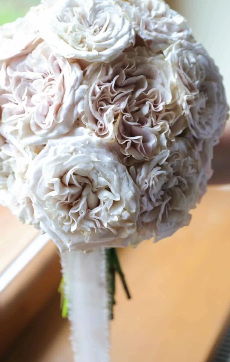 Bridal bouquet of blush and cream roses with full, ruffled petals wrapped in white ribbon
