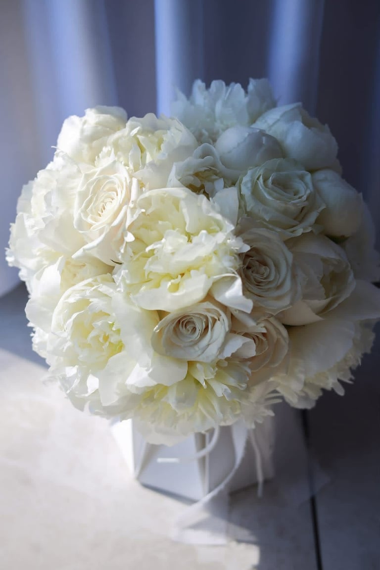 Bridal bouquet with white and cream roses and peonies in a white cube vase