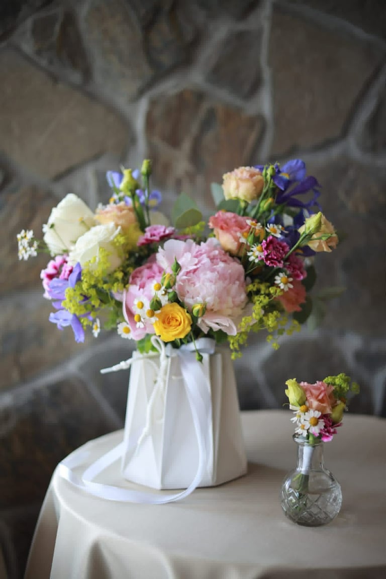 Colorful wedding flower arrangement in white pitcher with pink peonies, yellow roses, and purple flowers