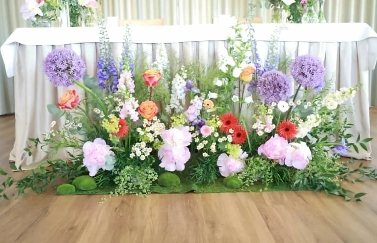 Large floral arrangement with purple, pink, red, and orange flowers arranged in front of a white draped table at an event