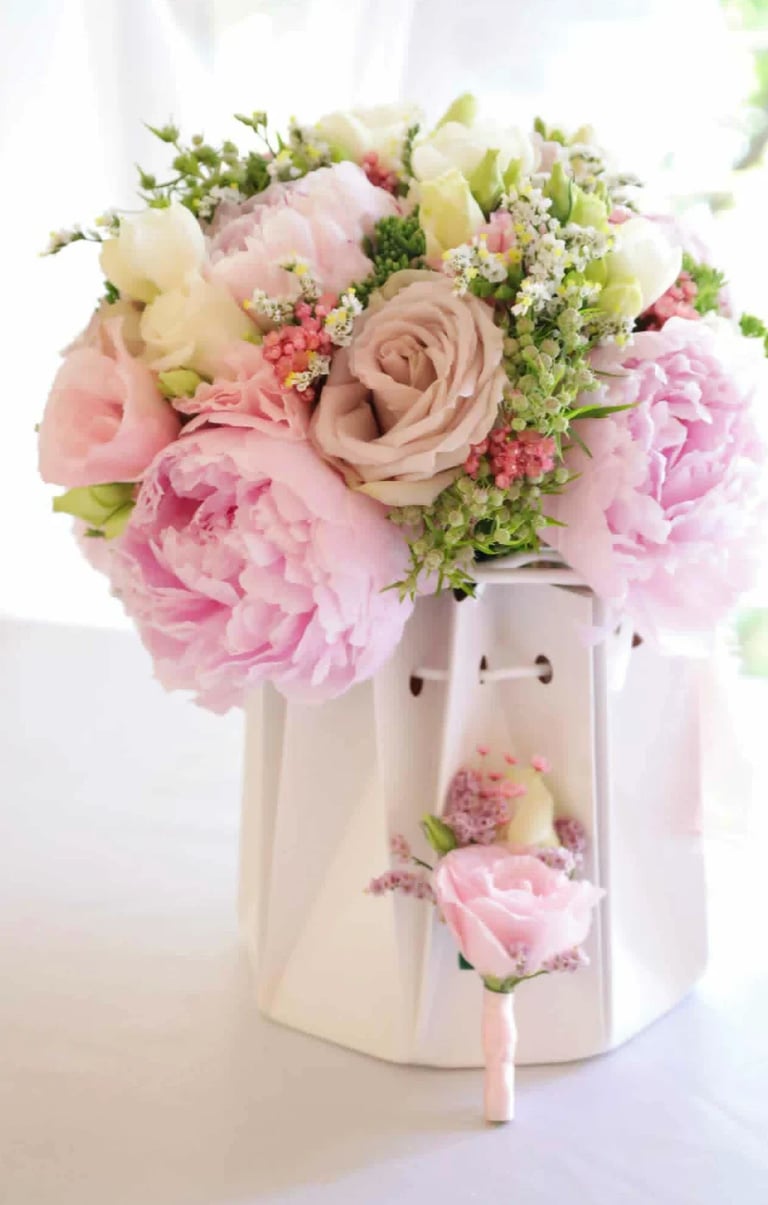 Pink and cream flower arrangement in white ceramic vase with peonies, roses, and babys breath on white background
