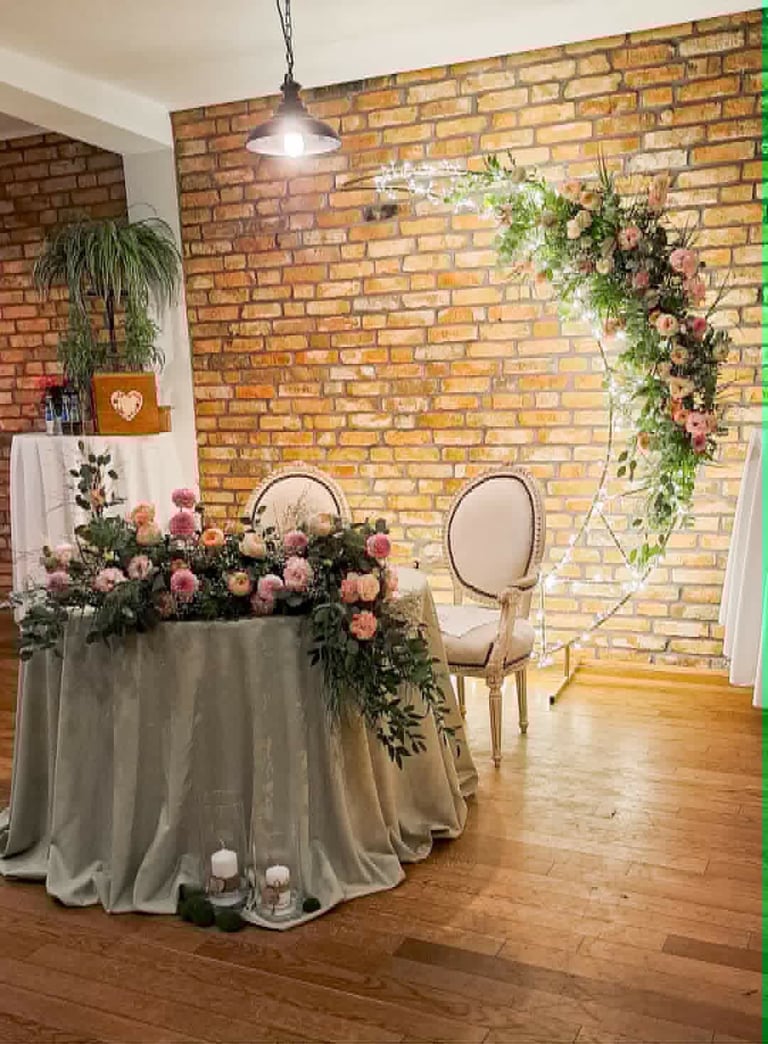 Elegant wedding reception setup with floral centerpiece, draped table, and seating against exposed brick wall with pendant lighting