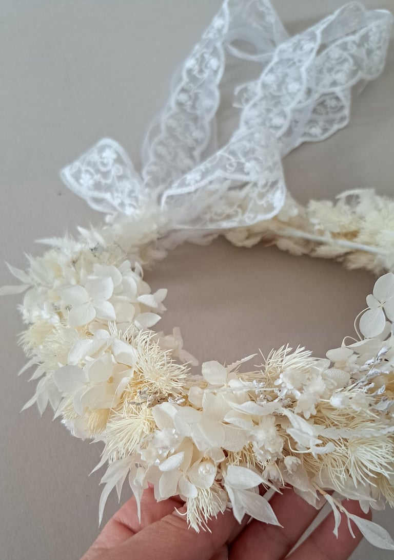 Delicate cream-colored decorative wreath made of dried flowers and grasses with a sheer white lace ribbon bow
