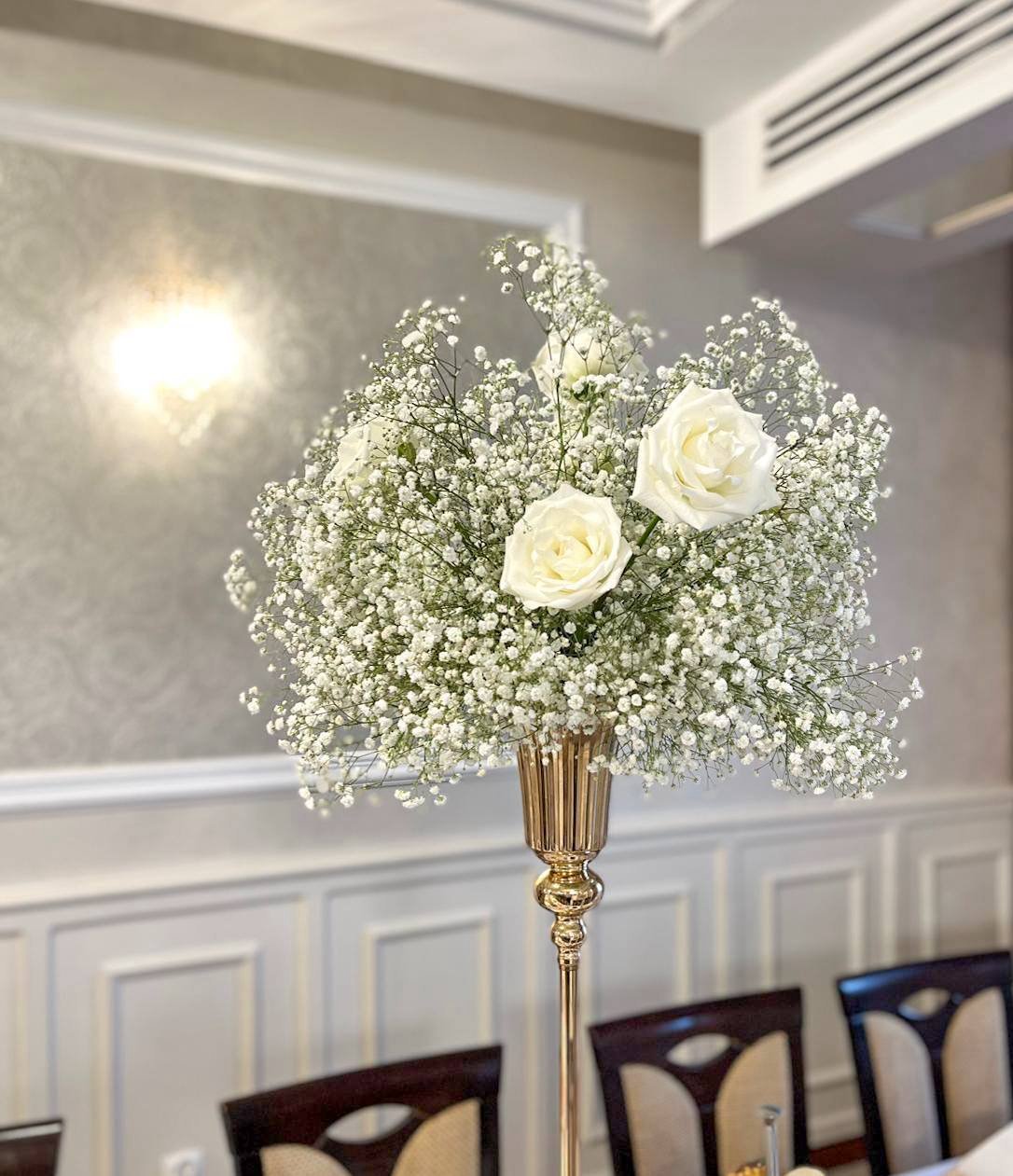 Elegant floral arrangement with white roses and babys breath in a gold vase on an event table