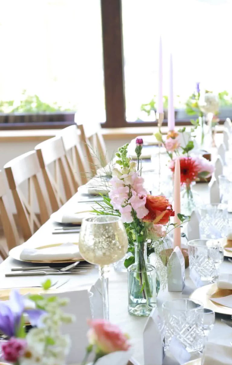 Elegant formal dining table with white linens, place settings, floral centerpieces, and glassware arranged for a special event